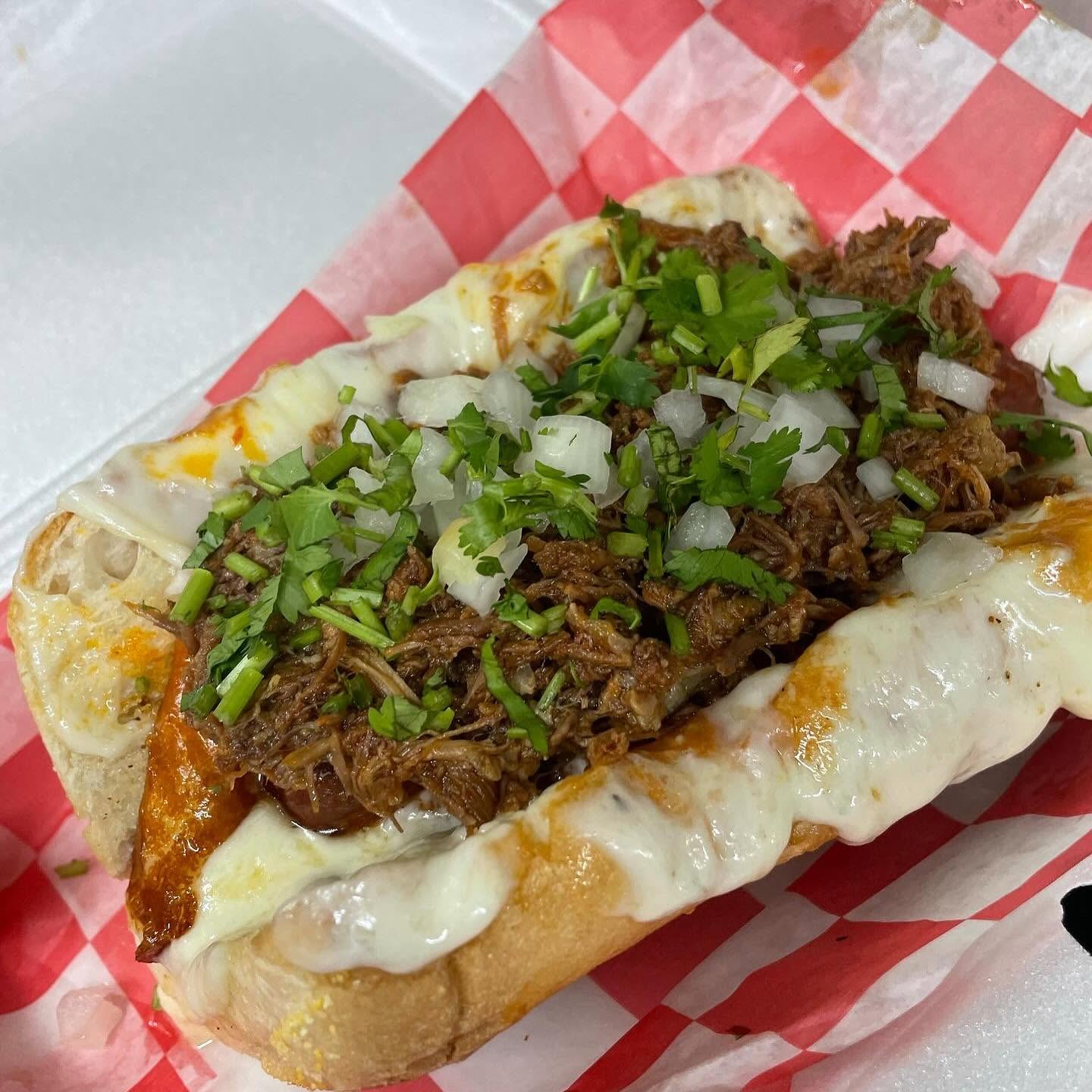 A birria torta loaded with melted cheese, shredded beef, onion and cilantro
