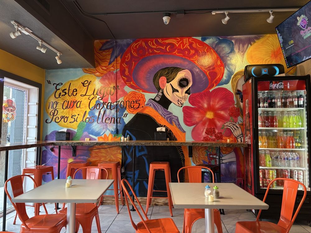 The colorful Catrina mural and orange seating inside Birriería Iturbidense